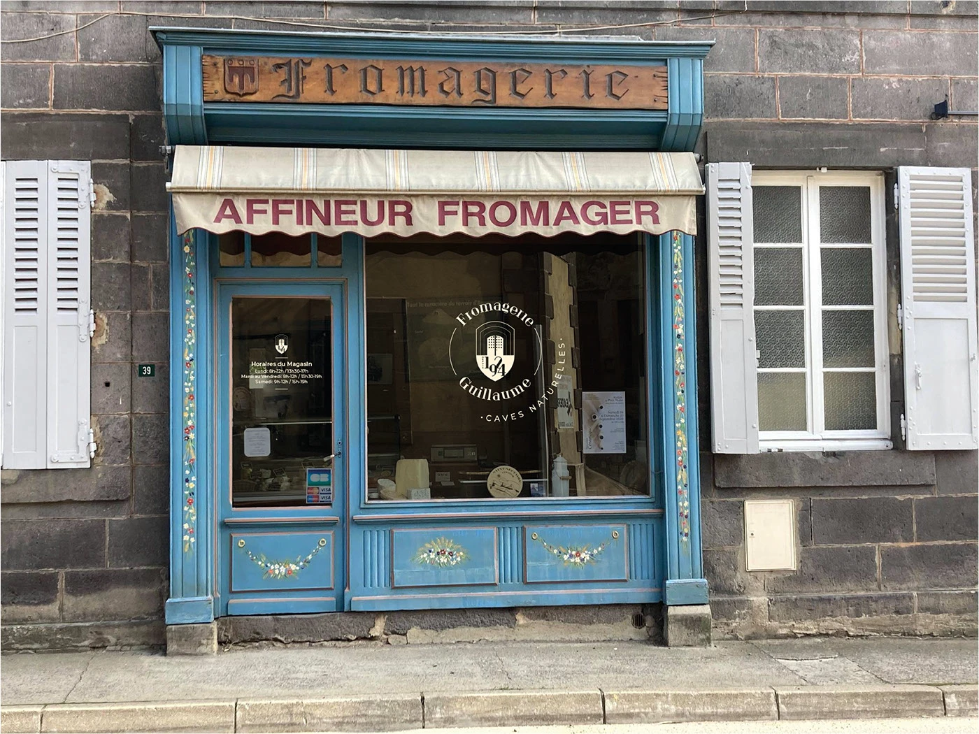 Devanture bleue de la Fromagerie Guillaume en portfolio, bandeau de bois Fromagerie, lambrequin Affineur fromager, médaillon Caves naturelles sur la vitrine et horaires sur la porte, maquette sans preuve de pose.