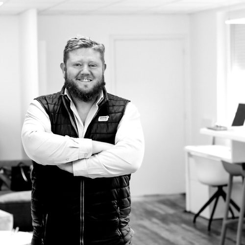 Portrait en noir et blanc de Dimitri Darrot, fondateur de l’agence Comm360, bras croisés dans un bureau.