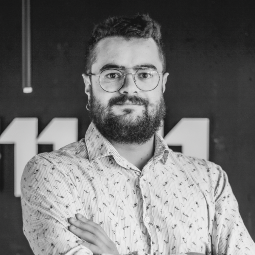 Portrait en noir et blanc de Hugo Cadeddu, cogérant de Comm360, devant un mur sombre portant un grand logo blanc.