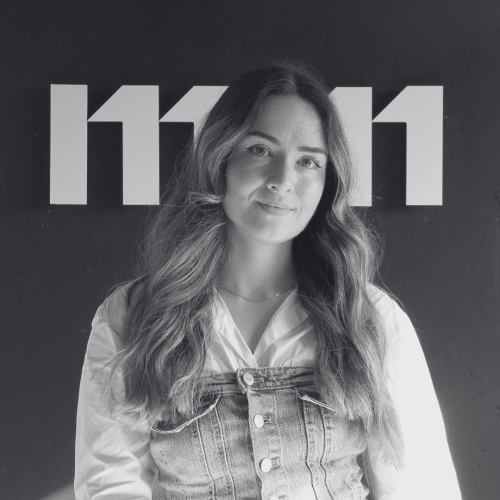 Portrait en noir et blanc de Lucie Pons, cheffe de projet chez Comm360, devant un mur sombre portant un grand logo blanc.